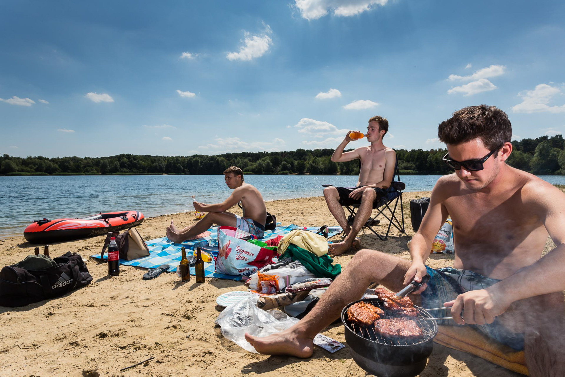 Jugendliche beim Baden und Grillen am Sandstrand eines Baggersees im Sommer